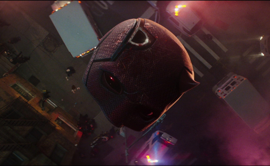 Close-up of Daredevil’s weathered mask with red lens in the foreground, with an upside-down urban street and vehicles in the background from Daredevil Born Again S1